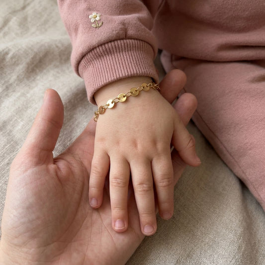 Children's Coin Bracelet worn on a child's wrist beneath a pink sleeve, with their hand resting in an adult's palm.