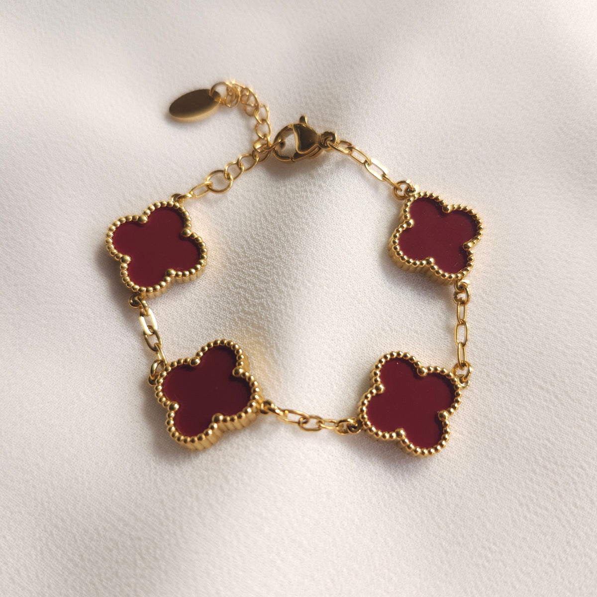 Children’s gold-tone bracelet with four burgundy clovers and beaded borders.
