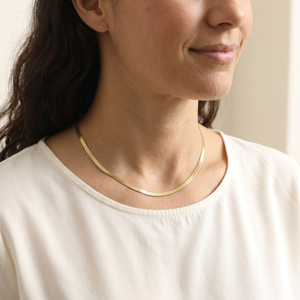 Classic Herringbone Necklace worn alone, showing the flat gold-tone chain resting around the neckline.
