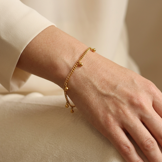 Close-up of a model wearing the gold-tone Dangling Dots Bracelet with a cream sleeve.