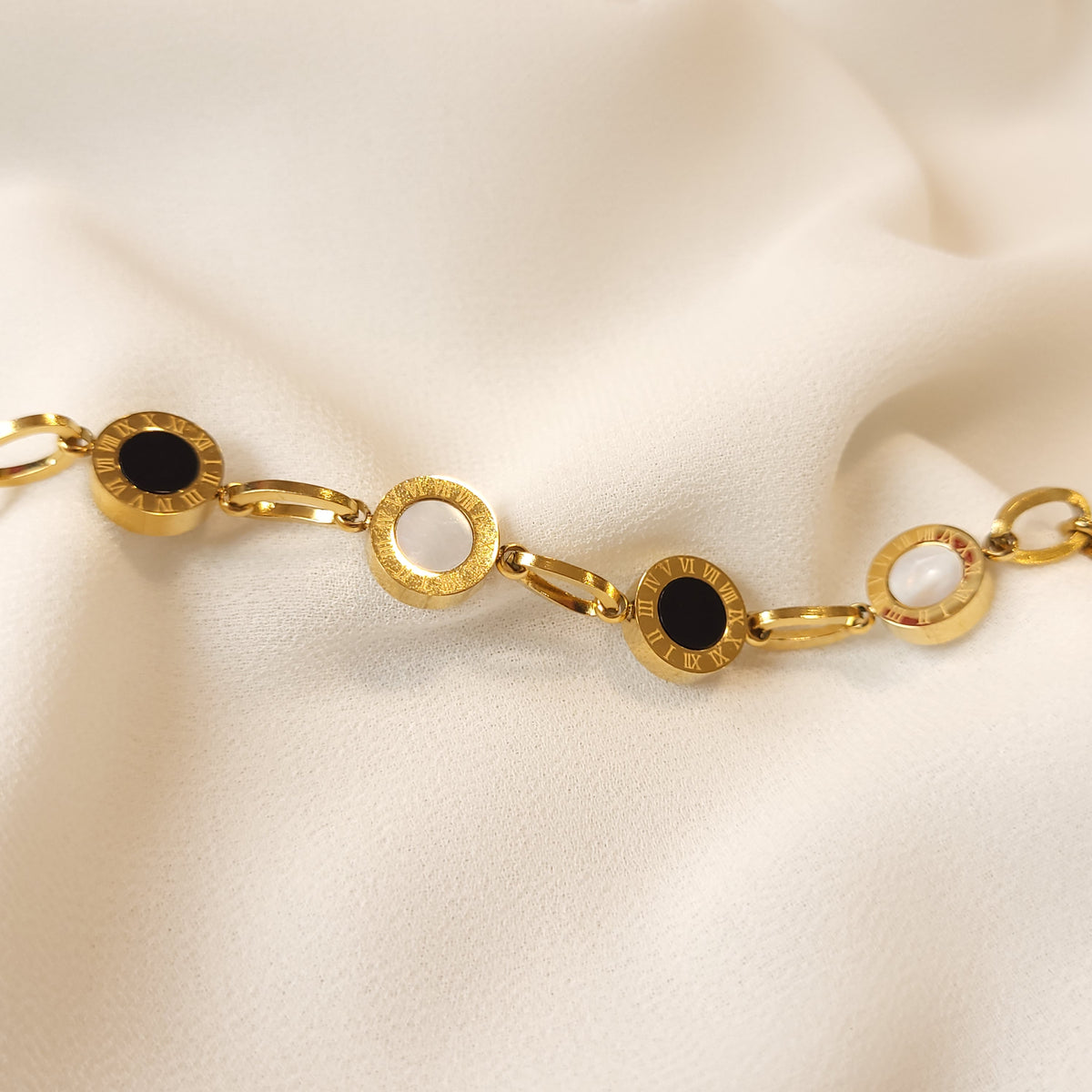 Close-up of the Roman Numeral Link Bracelet showing black and white centres framed by engraved gold-tone Roman numerals.