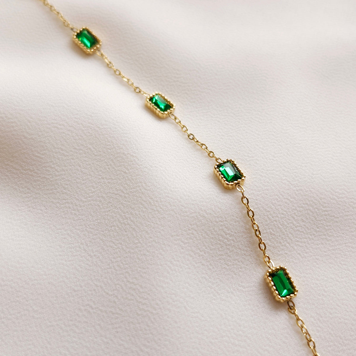 Close-up of the Satellite Emerald Bracelet showing rectangular green stones in gold beaded settings along a fine chain.