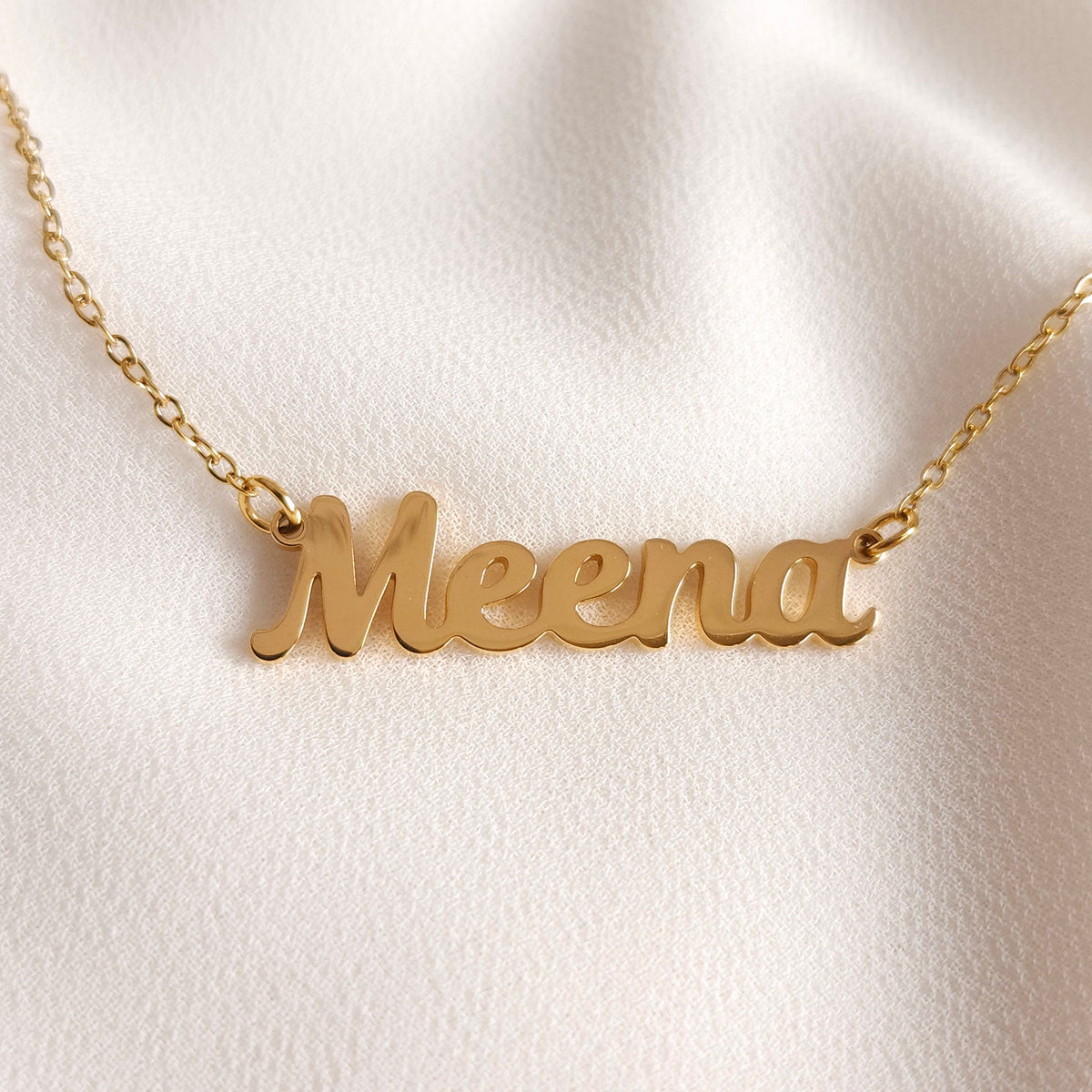 Close-up of the gold Meena name necklace showing its polished script lettering and chain connections.
