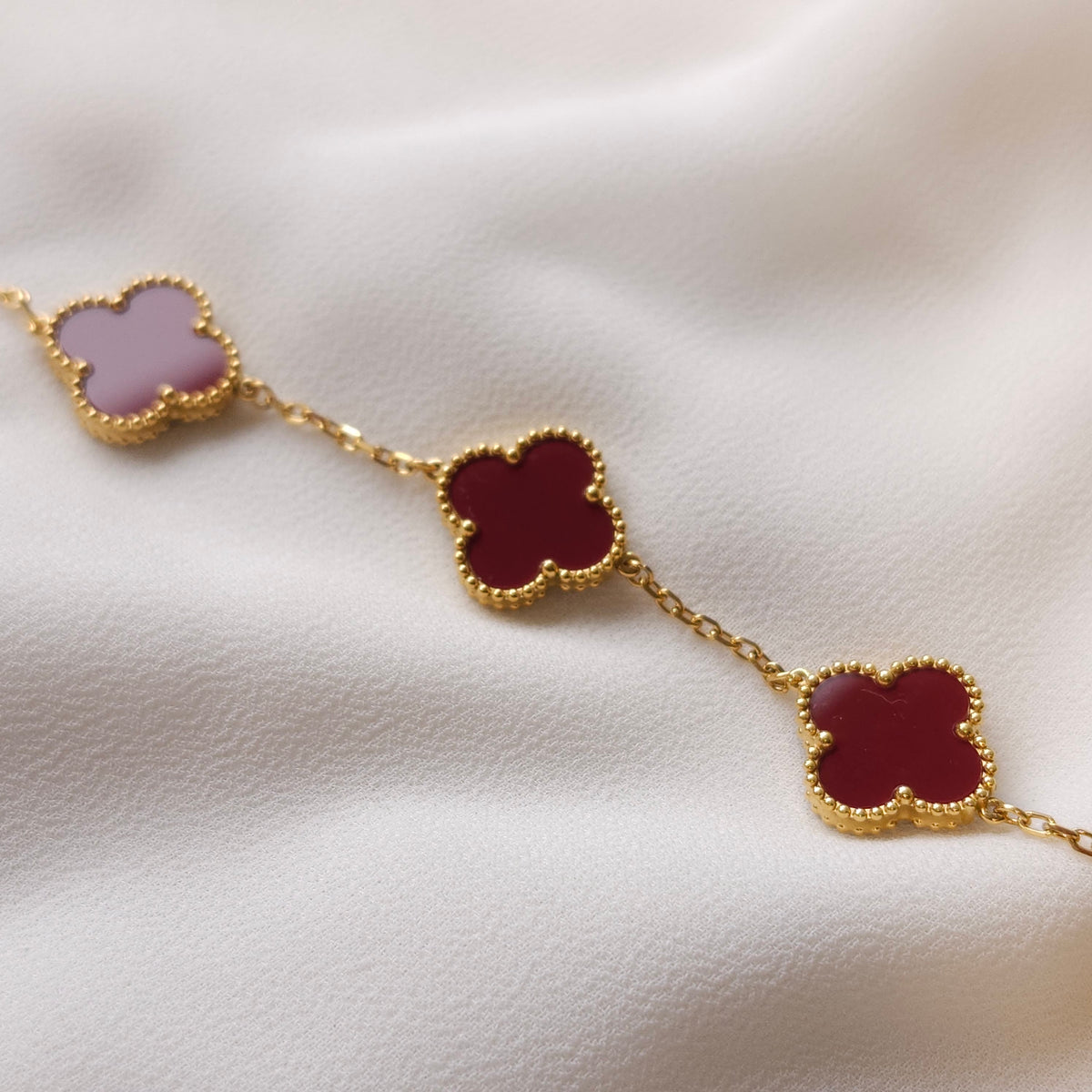 Close-up of the red Clover Bracelet showing clover charms with gold beaded borders connected by fine chain.