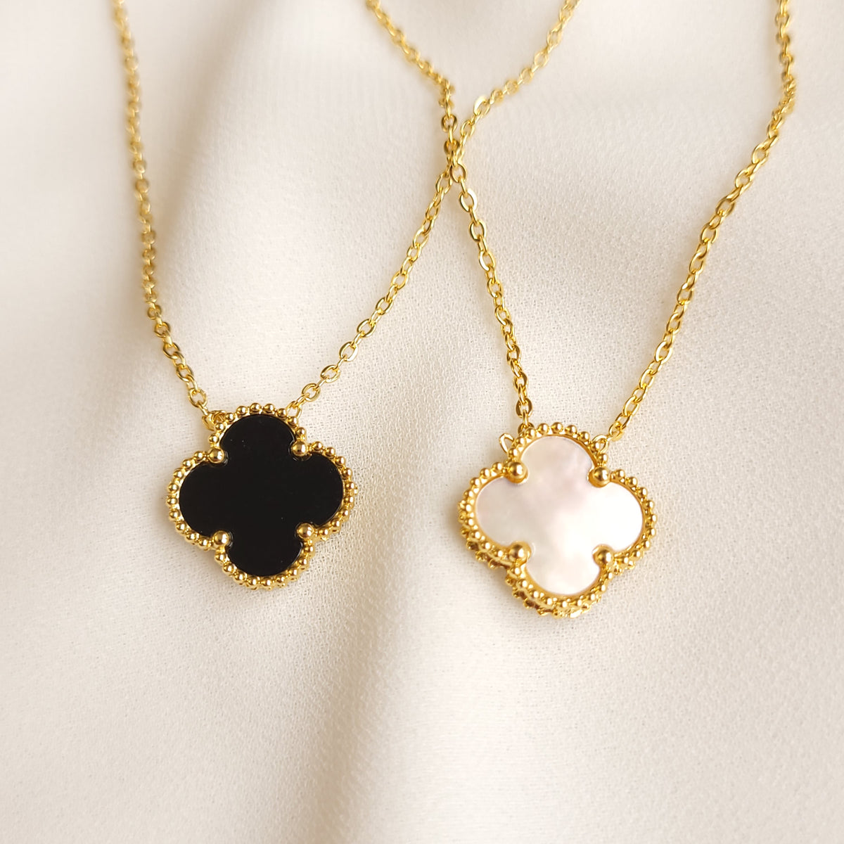 Clover Pendant Necklace in black and pearly white, showing both four-lobed pendants with gold-tone beaded borders and fine chains.