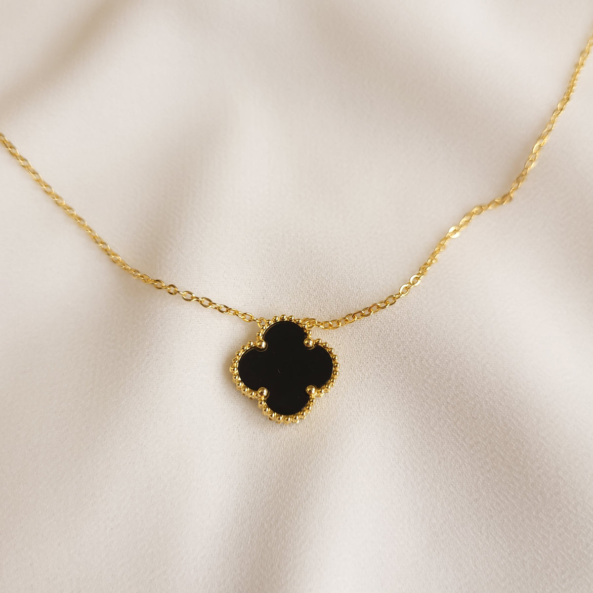 Clover Pendant Necklace in black, showing the polished four-lobed centre and gold-tone beaded edging.