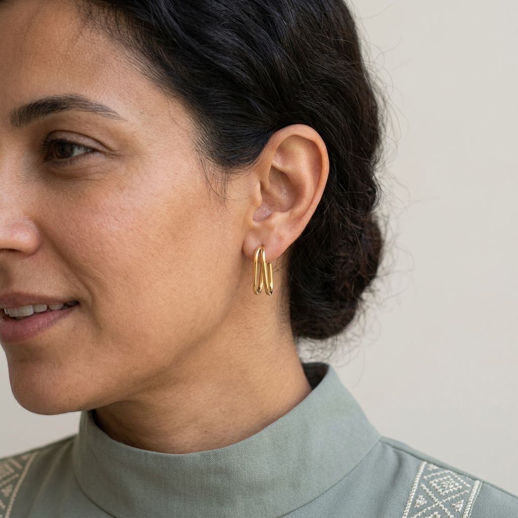 Double U-Hoop Earrings worn on an earlobe, showing the two slim gold-tone curves and short drop.