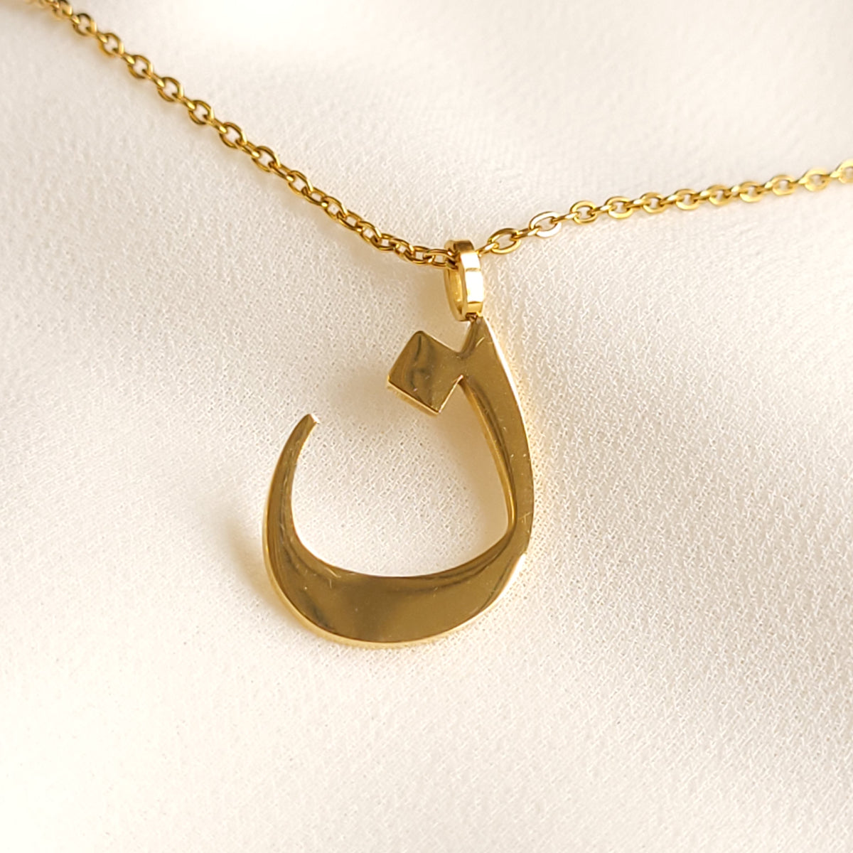 Gold-tone Arabic Initial Necklace with the letter Noon (ن) on cream fabric.