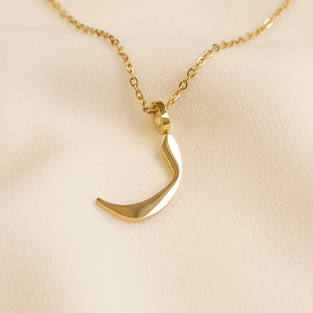Gold-tone Arabic Initial Necklace with the letter Raa (ر) on cream fabric.