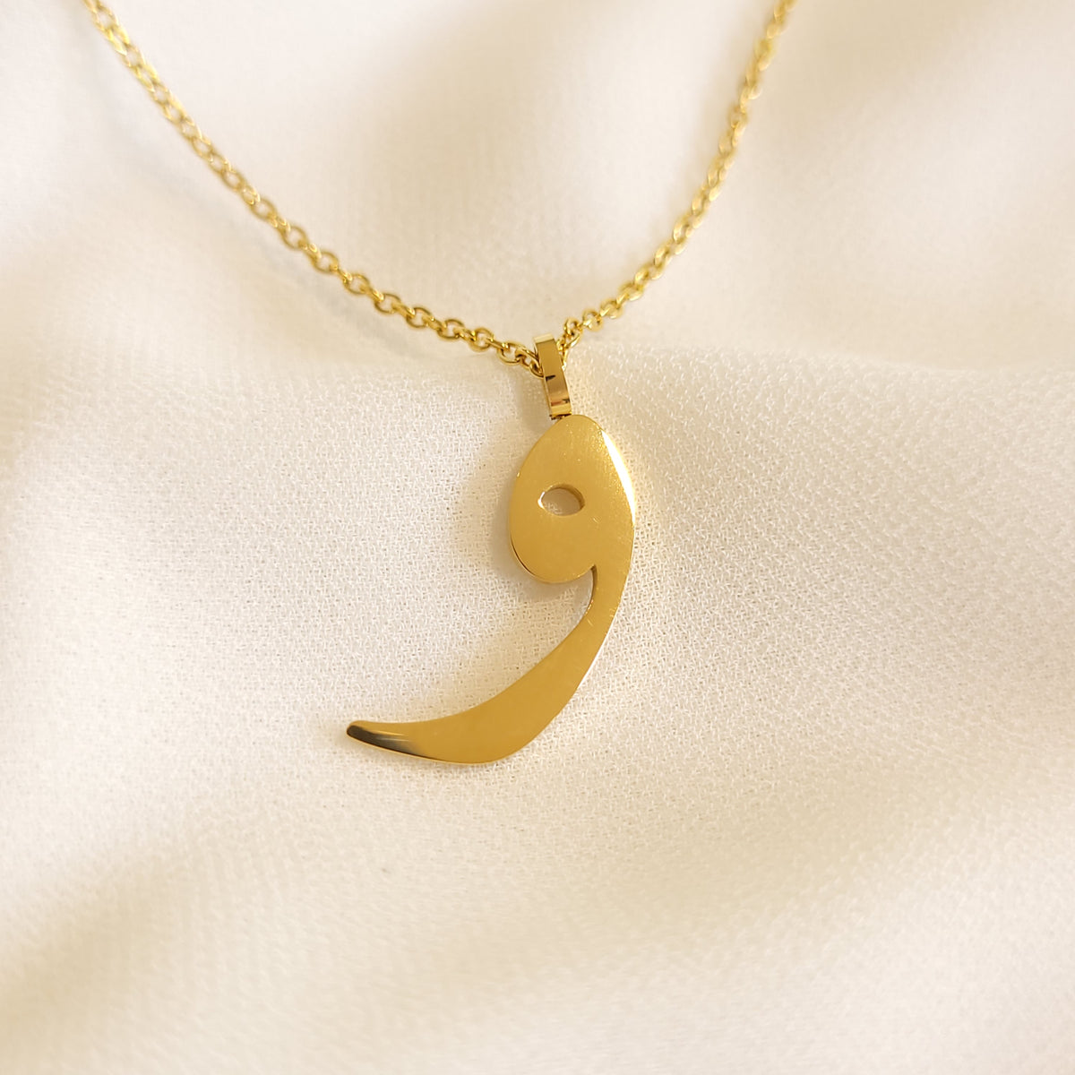 Gold-tone Arabic Initial Necklace with the letter Waw (و) on cream fabric.