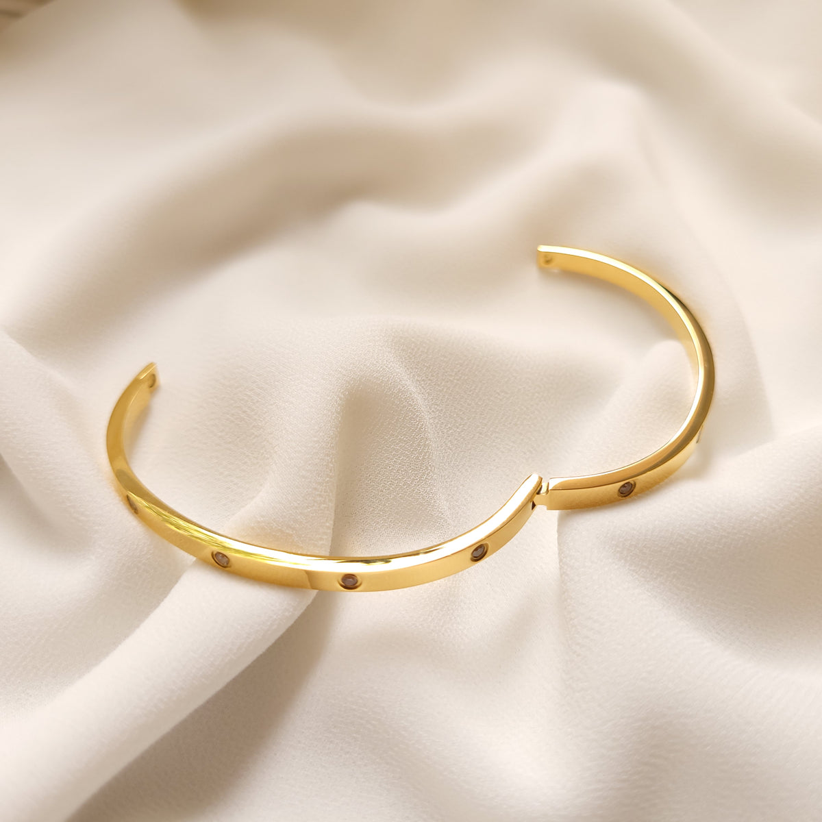 Gold-tone Crystal Stud Bangle opened to show its hinge and clasp on cream fabric.