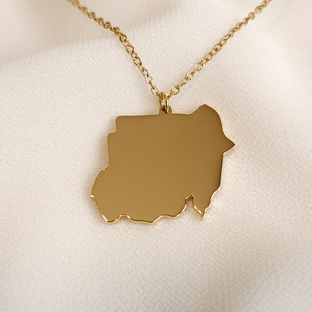 Gold-tone Sudan map pendant necklace displayed at an angle.