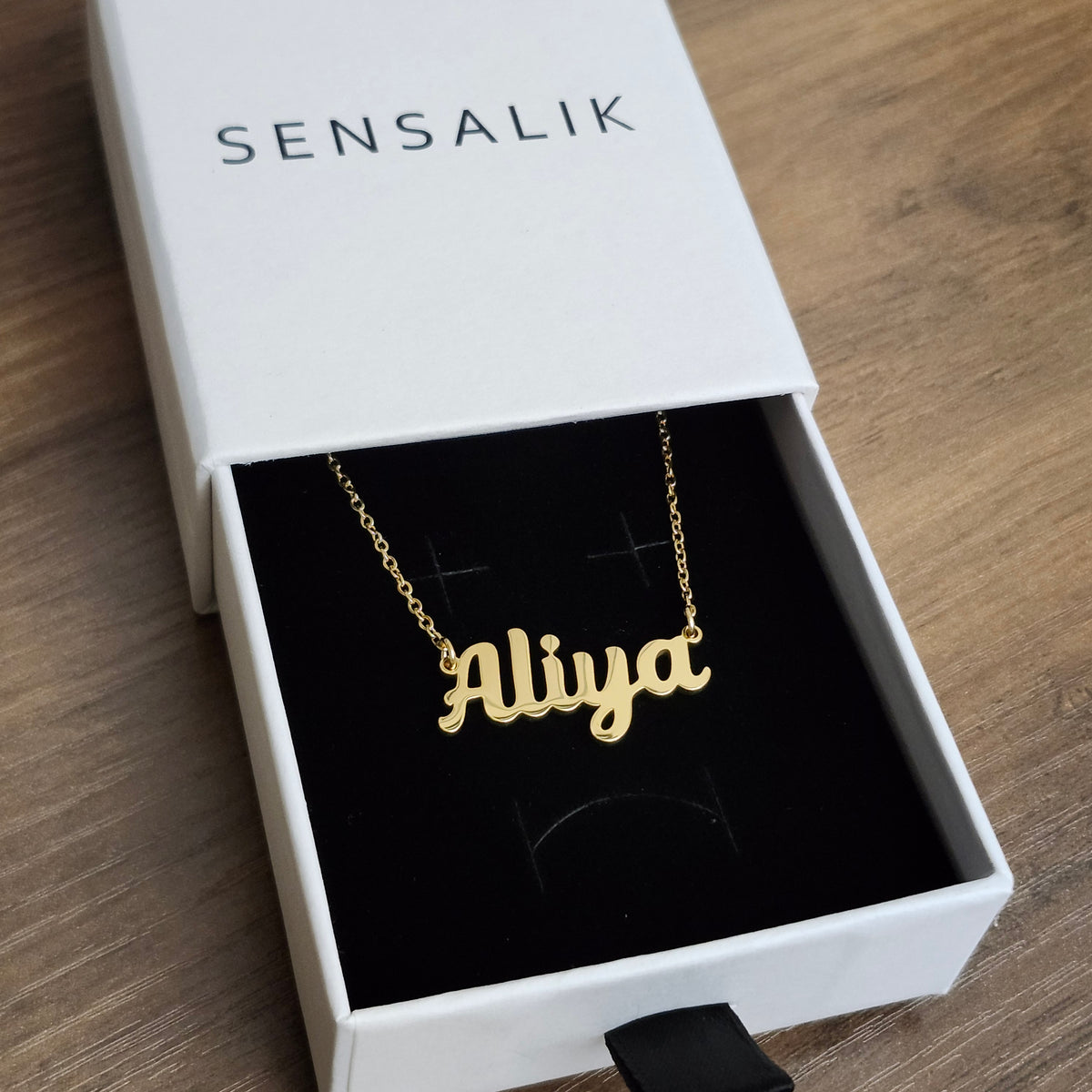 Gold Aliya script name necklace displayed in a Sensalik gift box.