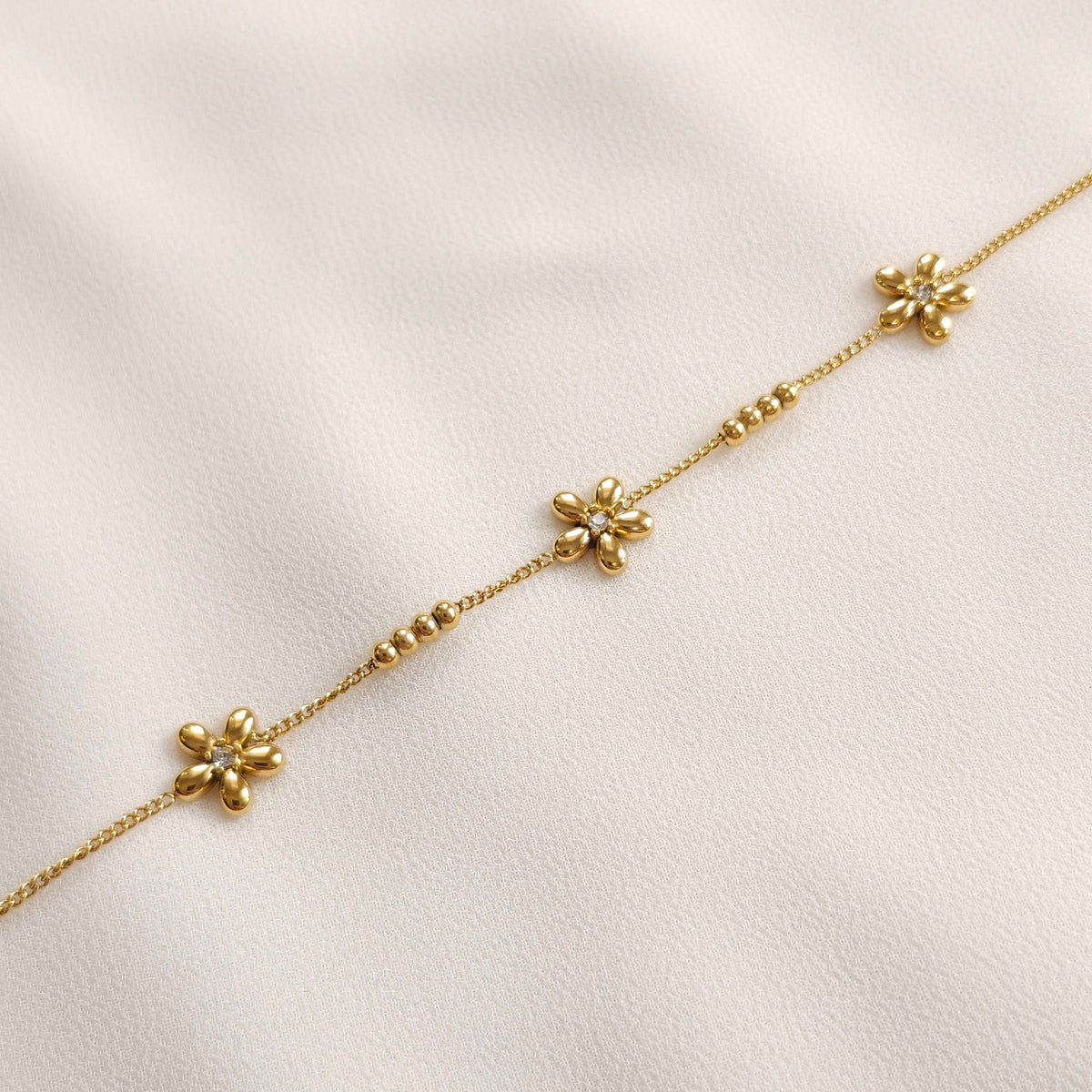 Gold Daisy Chain Bracelet laid straight, showing three polished flowers with clear centres along a fine chain.