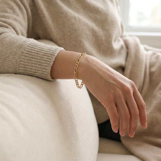 Gold Figaro bracelet worn on a model’s wrist, showing its alternating short and elongated links.