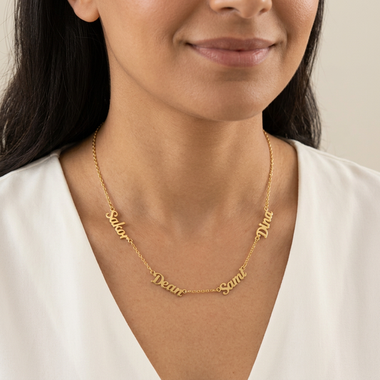 Model wearing a gold Multiple Name Necklace with four script nameplates spaced along the chain.