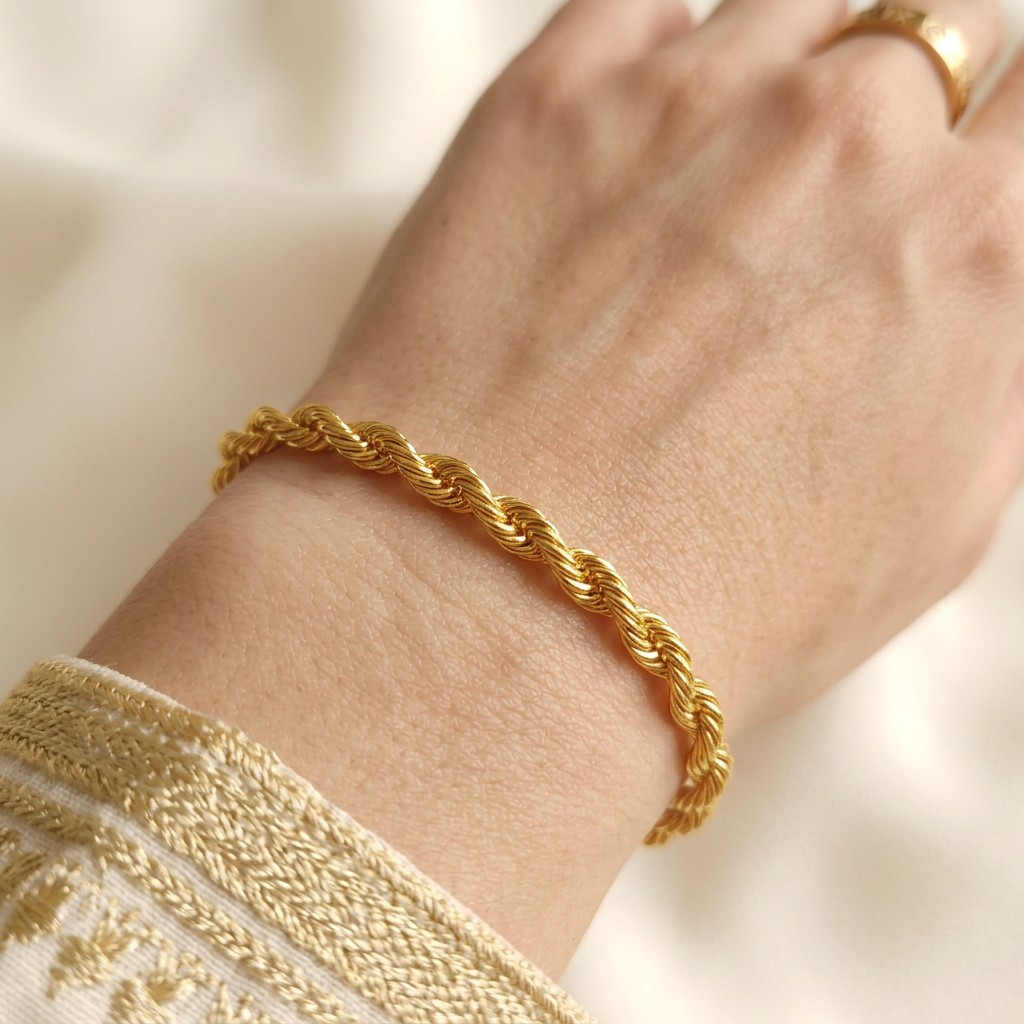 Rope Bracelet worn on a wrist, showing the polished gold-tone twists beside an embroidered cuff and gold-tone ring.
