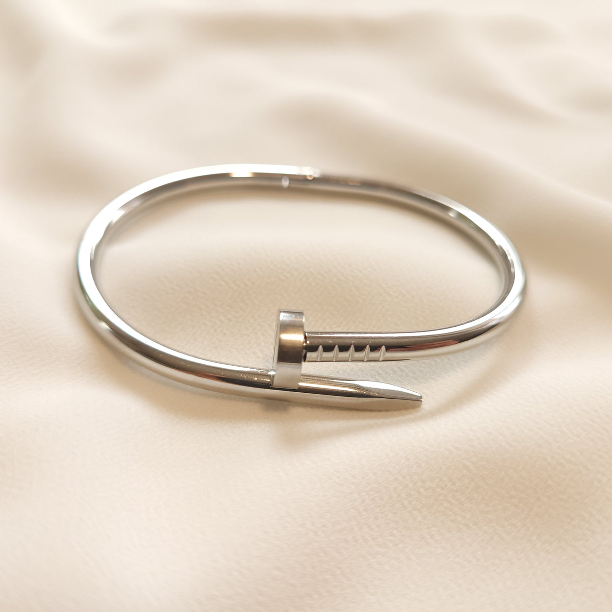 Twisted Nail Bangle in silver tone, showing the overlapping nail head, engraved lines, and tapered tip.