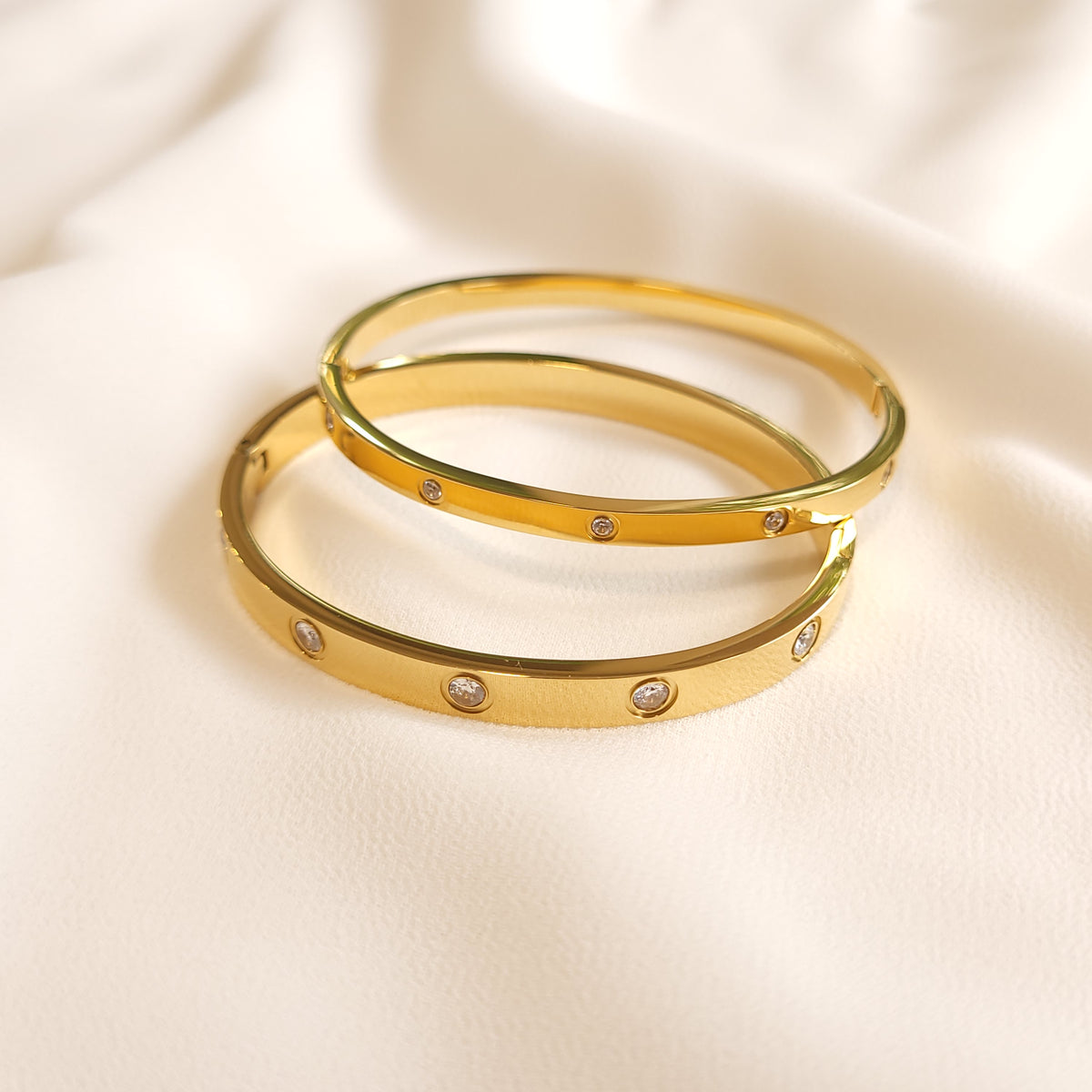 Two gold-tone Crystal Stud Bangles with narrow and wide bands and round clear stones.