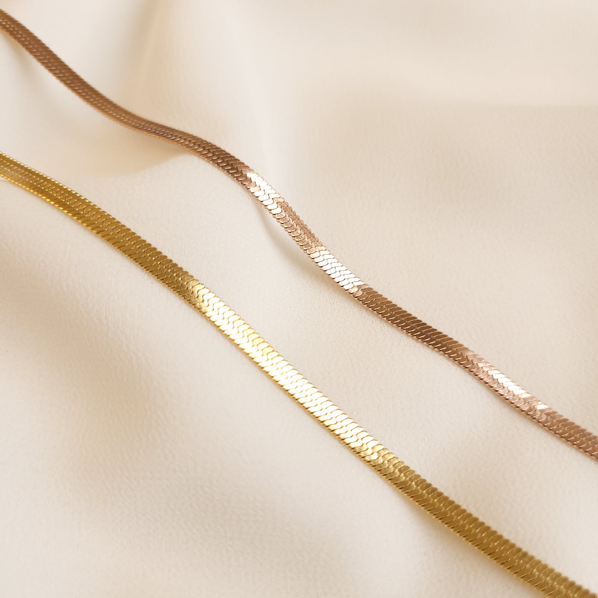 Classic Herringbone Necklaces in gold and rose gold tones shown side by side, highlighting their fine woven texture.