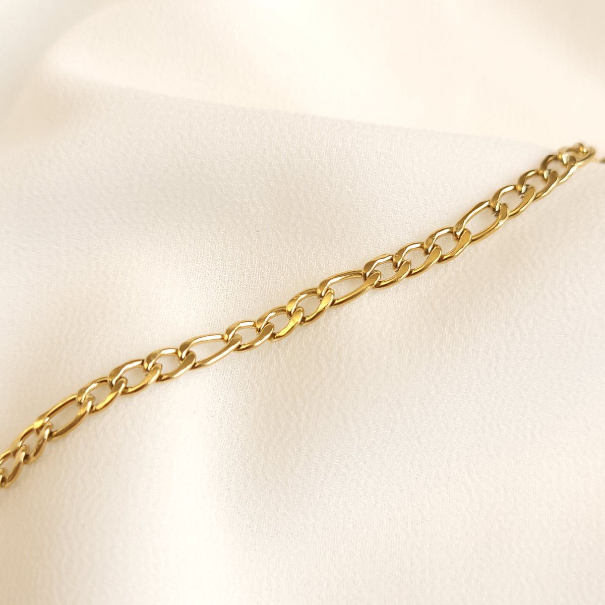 Close-up of a gold Figaro bracelet showing three short links alternating with one elongated link.