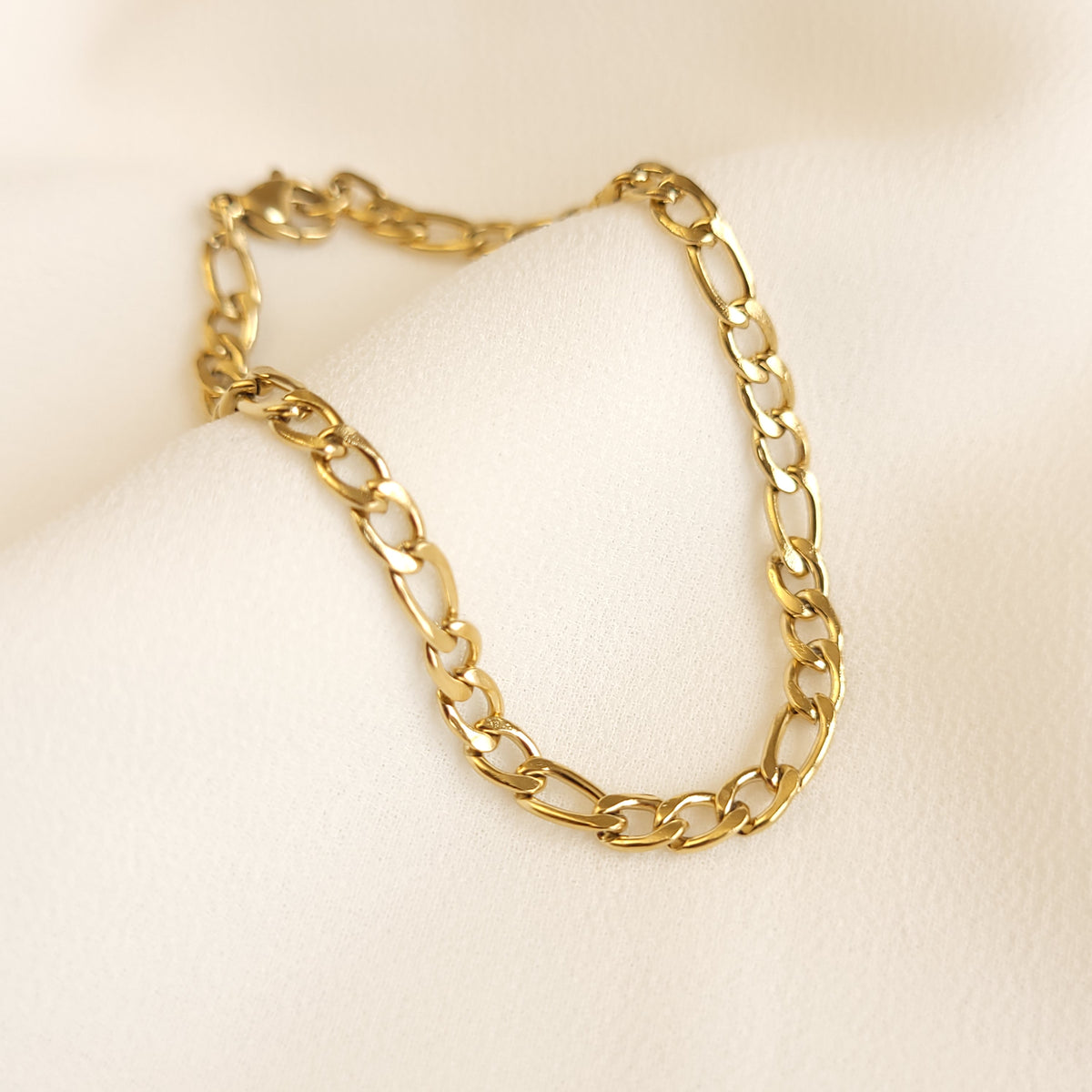 Gold Figaro bracelet with a repeating pattern of three short links and one elongated link.