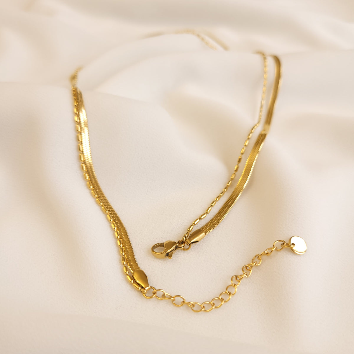 Herringbone and Oval Bead Necklace fastening detail showing the lobster clasp, extension chain, and heart-shaped end tag.