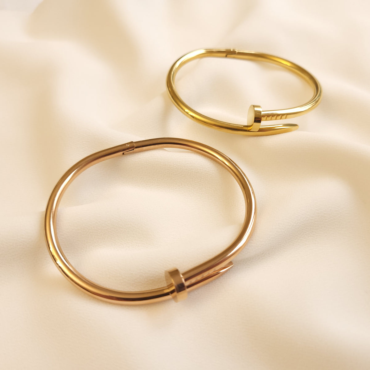 Twisted Nail Bangles in gold and rose gold tones arranged separately, showing their oval shape and hinged bands.