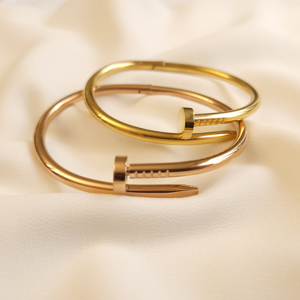 Twisted Nail Bangles in gold and rose gold tones overlapped to compare their finishes and nail-shaped details.