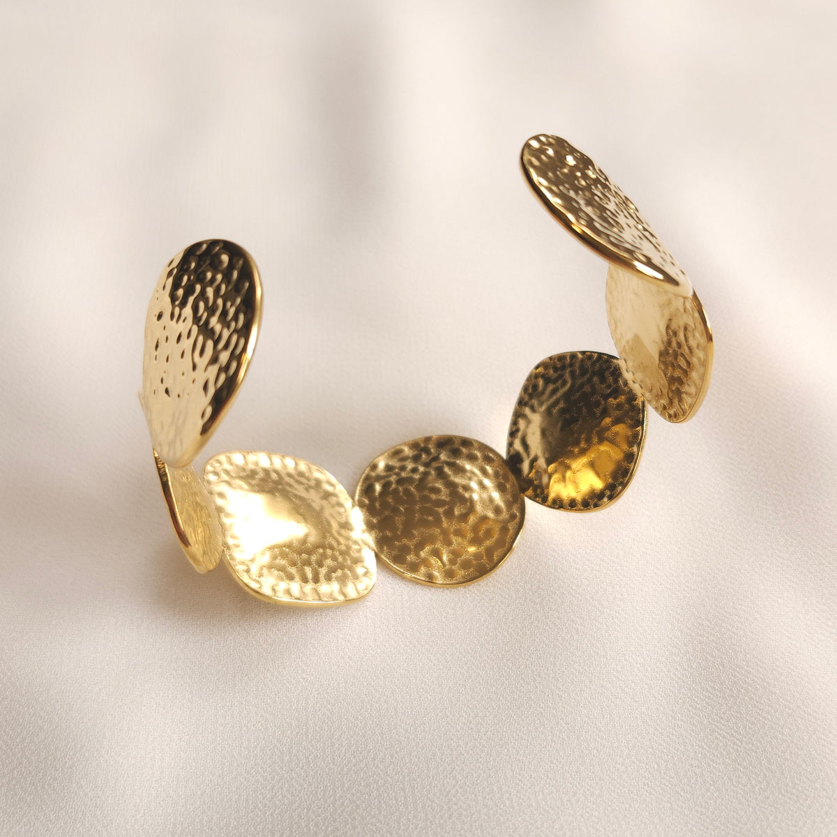 Angled view of the gold Bold Disc Cuff showing the hammered texture of its round discs.