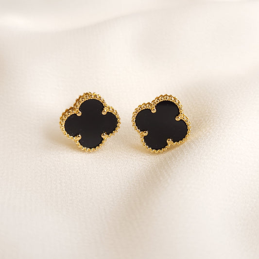 Black Clover Stud Earrings with four-lobed centres and beaded gold-tone borders on cream fabric.
