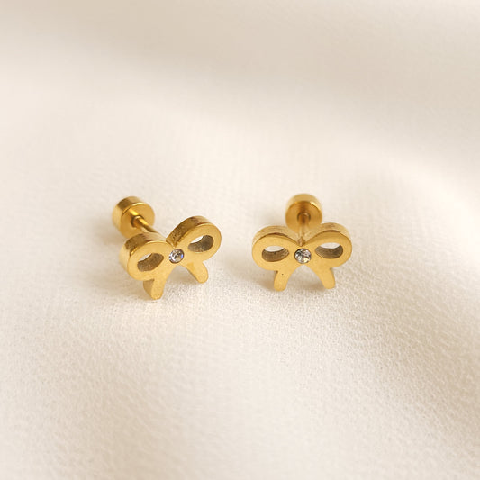 Bow Tie Stud Earrings worn on an earlobe, with auburn hair tied back to reveal the small gold-tone bow design.