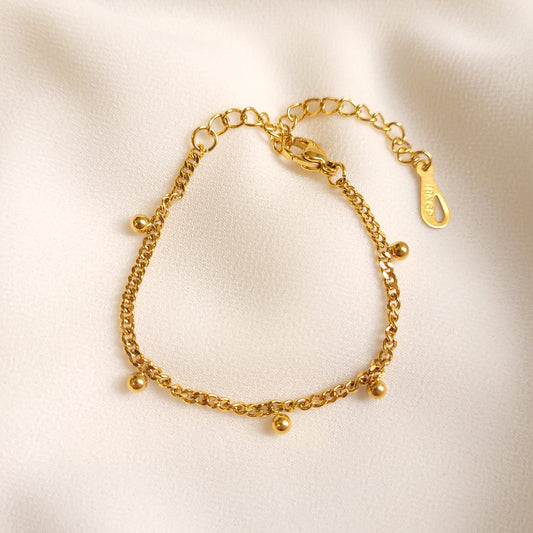 Children's Dangling Dots Bracelet arranged in a circle, featuring a gold-tone curb chain with small dangling ball charms.

