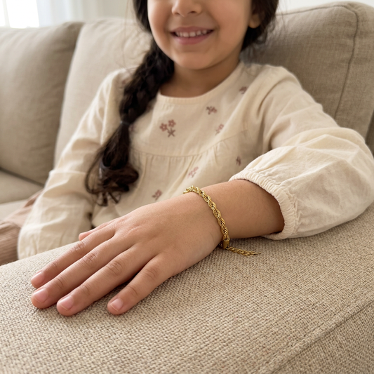 Children's Rope Bracelet worn on a child's wrist, with their hand resting on a sofa arm beside a cream floral sleeve.