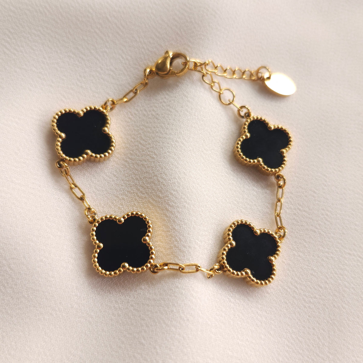 Children’s gold-tone bracelet with four black clovers and beaded borders on cream fabric.
