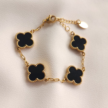 Children’s gold-tone bracelet with four black clovers and beaded borders on cream fabric.
