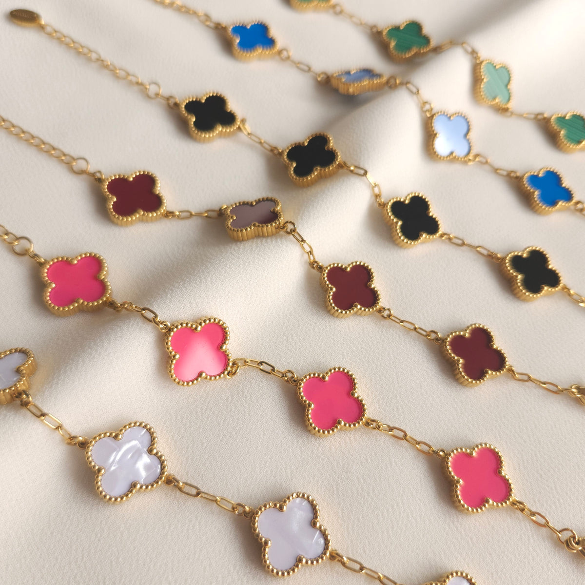 Children’s gold-tone clover bracelets in assorted colours arranged in rows on cream fabric.