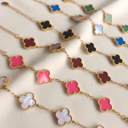 Children’s gold-tone clover bracelets in assorted colours arranged in rows on cream fabric.
