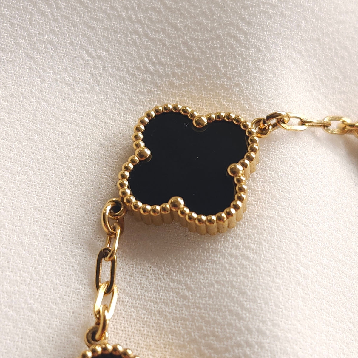 Close-up of a black clover with a gold-tone beaded border and oval chain links.