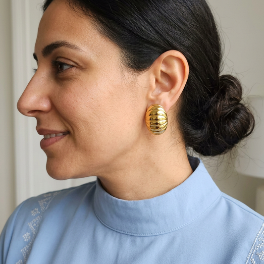 Close-up of a model wearing gold Bold Dome Earrings, showing their ribbed oval shape and fit against the earlobe.

