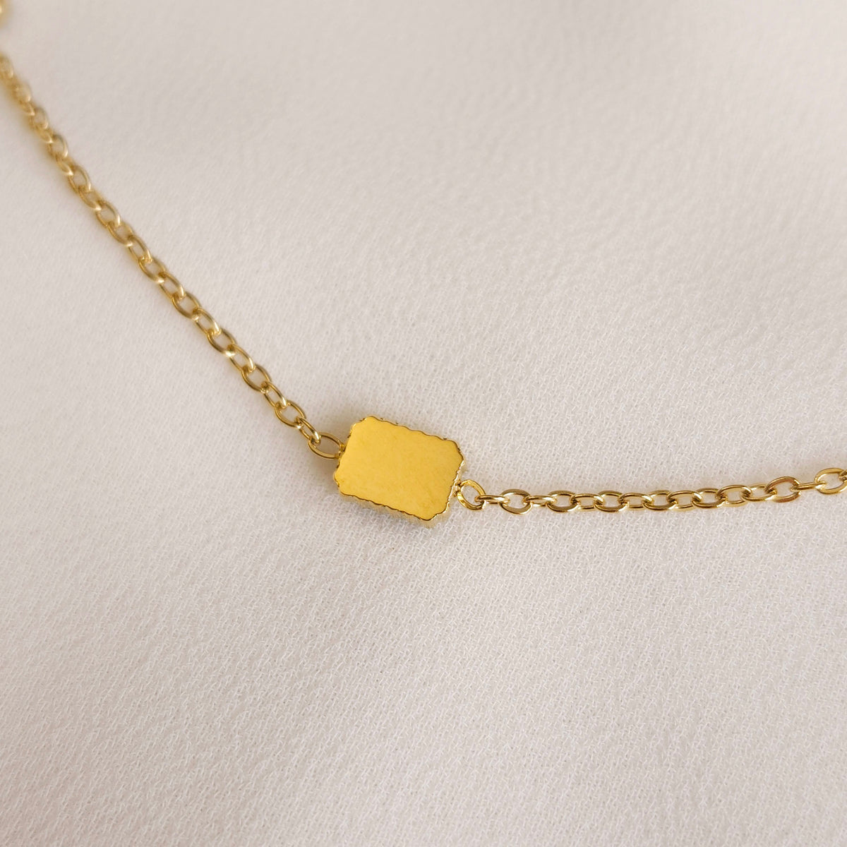 Close-up of a smooth rectangular gold setting back and its chain connections on the Satellite Emerald Bracelet.
