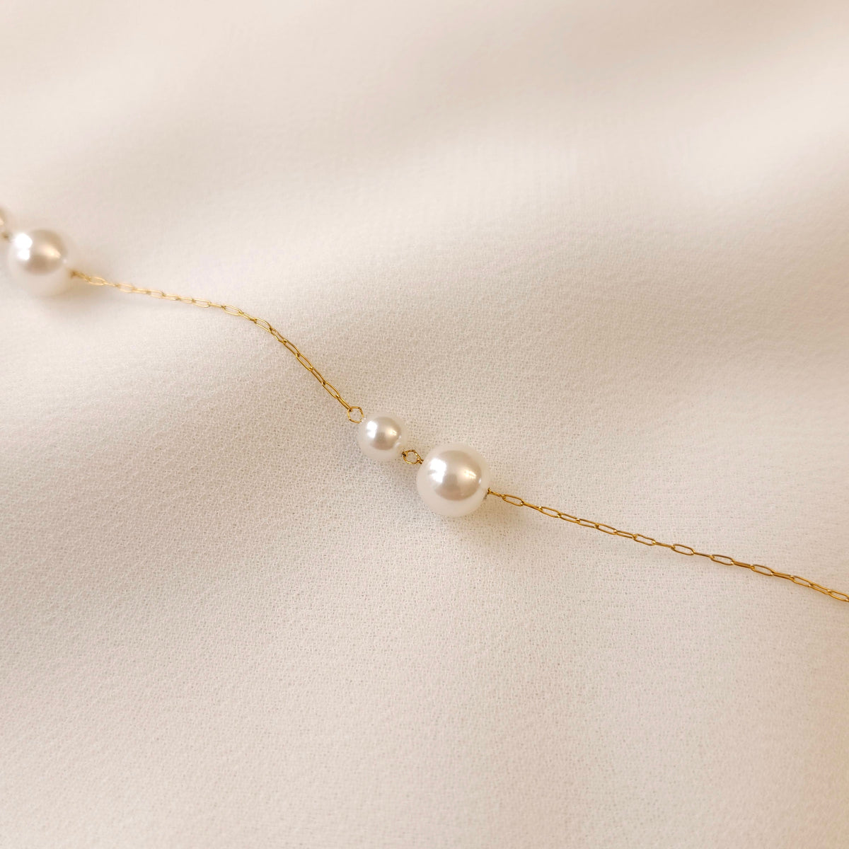 Close-up of the Doubled Up Pearl Bracelet showing a small and large white pearl paired along a fine gold chain.
