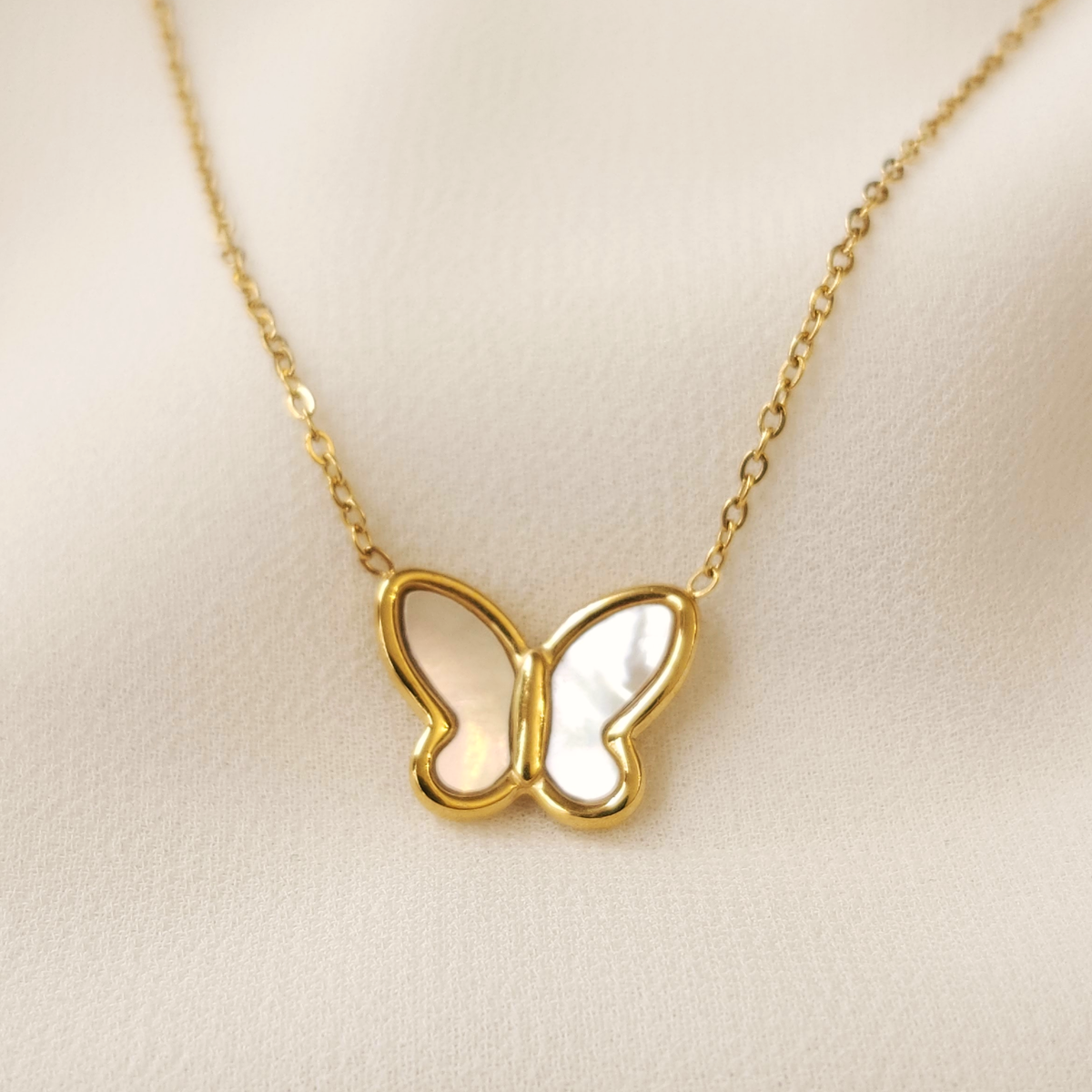 Close-up of the Mother of Pearl butterfly pendant showing pearly white wings framed in polished gold.
