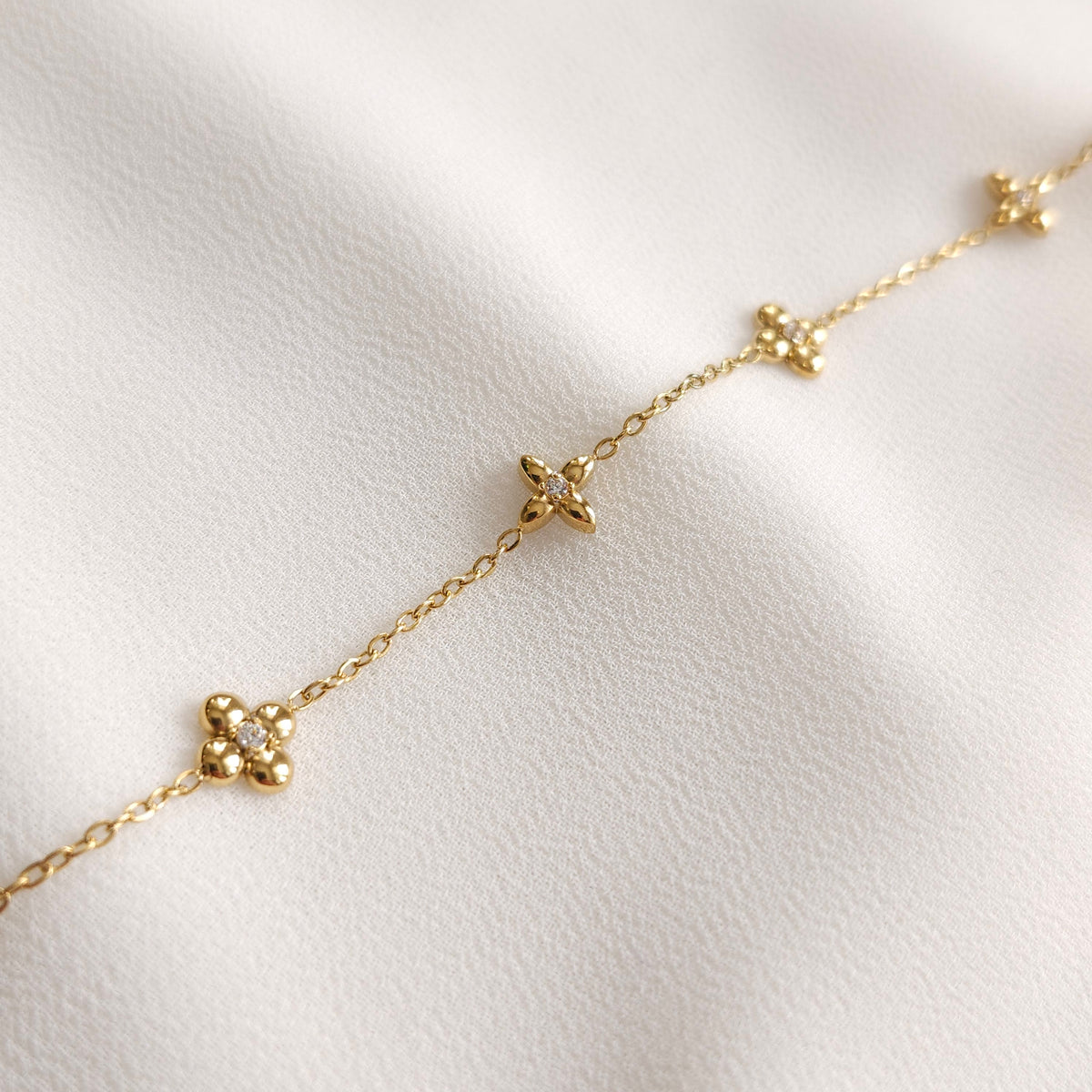Close-up of the gold Dainty Flower Bracelet showing rounded and pointed floral charms with clear stone centres