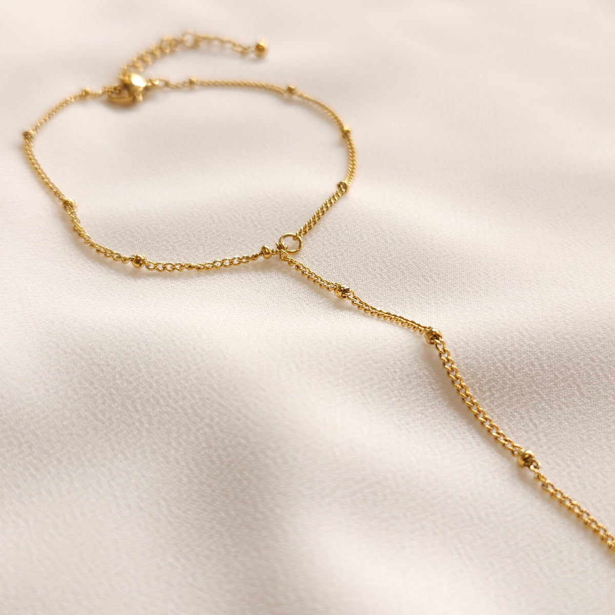 Close-up of the gold Dainty Hand Chain showing its small beads, wrist chain and central connecting ring.
