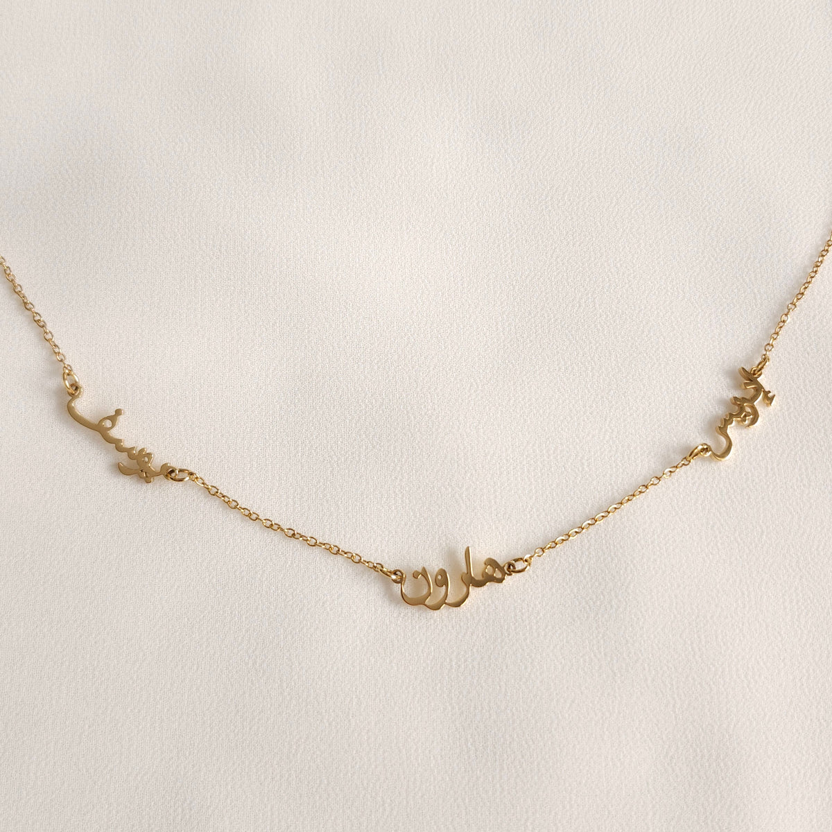 Close-up of three gold Arabic nameplates connected by sections of fine chain.
