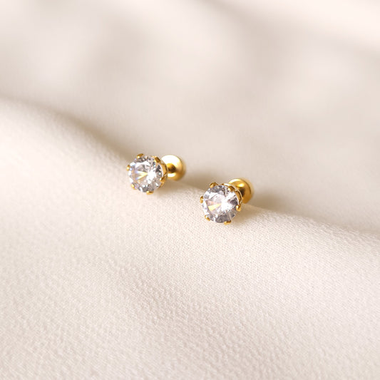 Crystal Stud Earrings with round clear stones in gold-tone prong settings on cream fabric.
