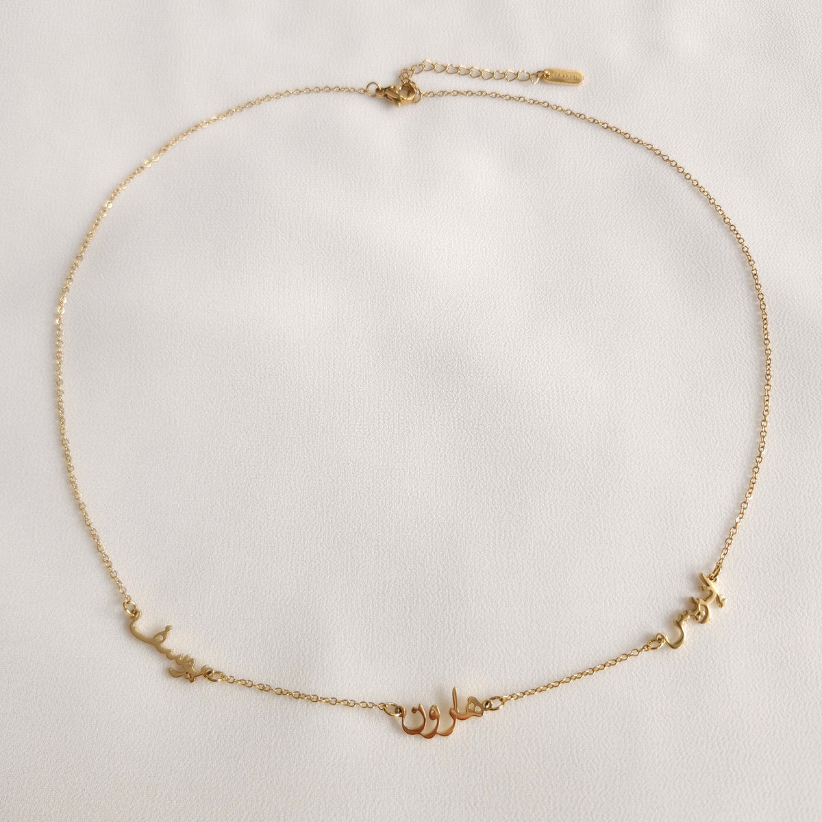 Full view of the gold Multiple Name Necklace with three Arabic nameplates, a lobster clasp and extension chain.
