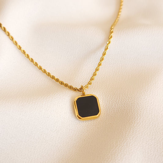 Geometric Black Stone Pendant with a square black centre, clipped corners and a gold-tone frame on a rope chain.
