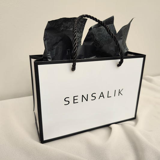 Gift Bag in white with black borders, twisted black rope handles, Sensalik lettering, and black tissue paper.